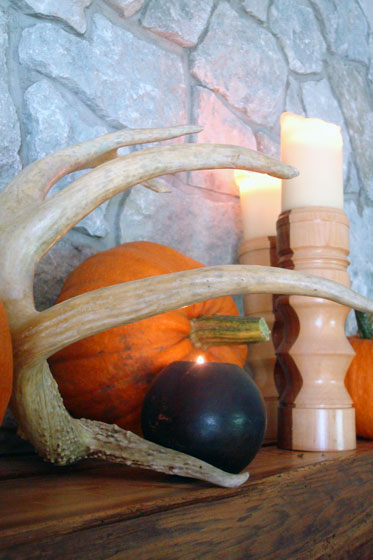 Antler, pumpkins and candles decorating a fall mantel