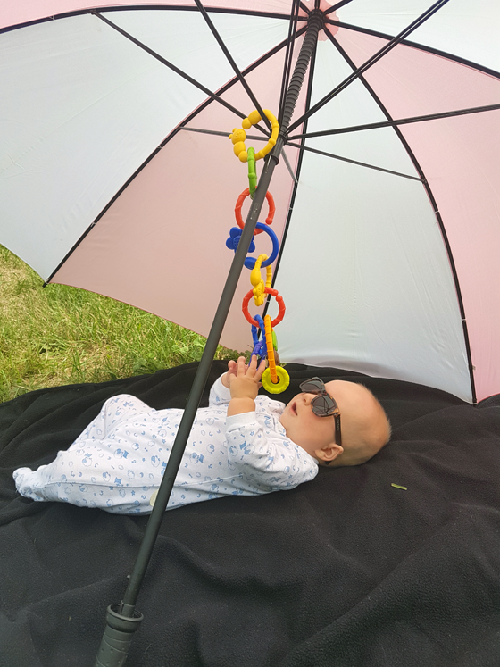 Baby wearing sunglasses lying outside under an umbrella