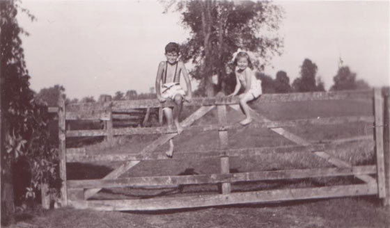 Black and white photo of two children sitting on top of a wood gate
