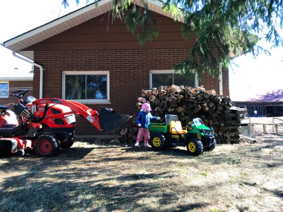 Two tractors (one a toy) in front of a pile of firewood