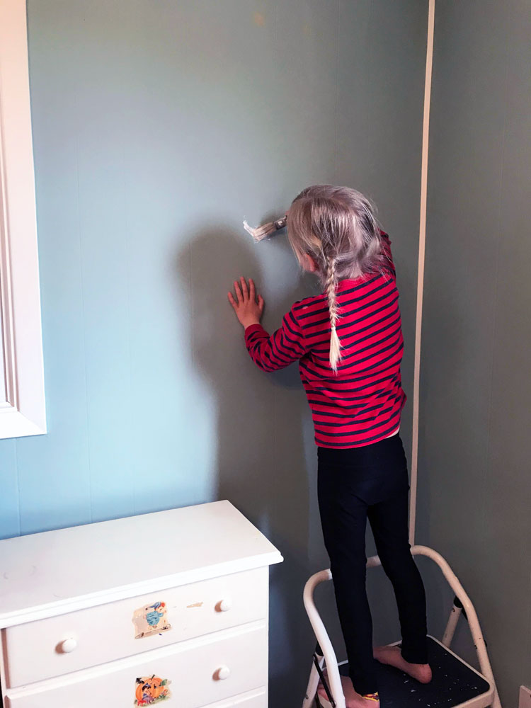 Child painting a wall while standing on a small ladder