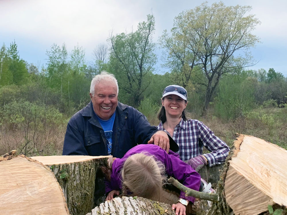 Man and woman smiling while standing behind a pile of large logs