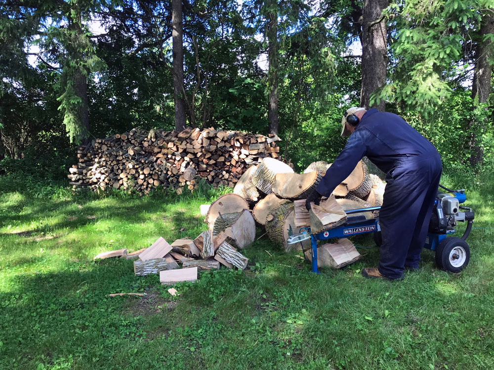 Man splitting logs with a wood splitter in front of a pile of firewood