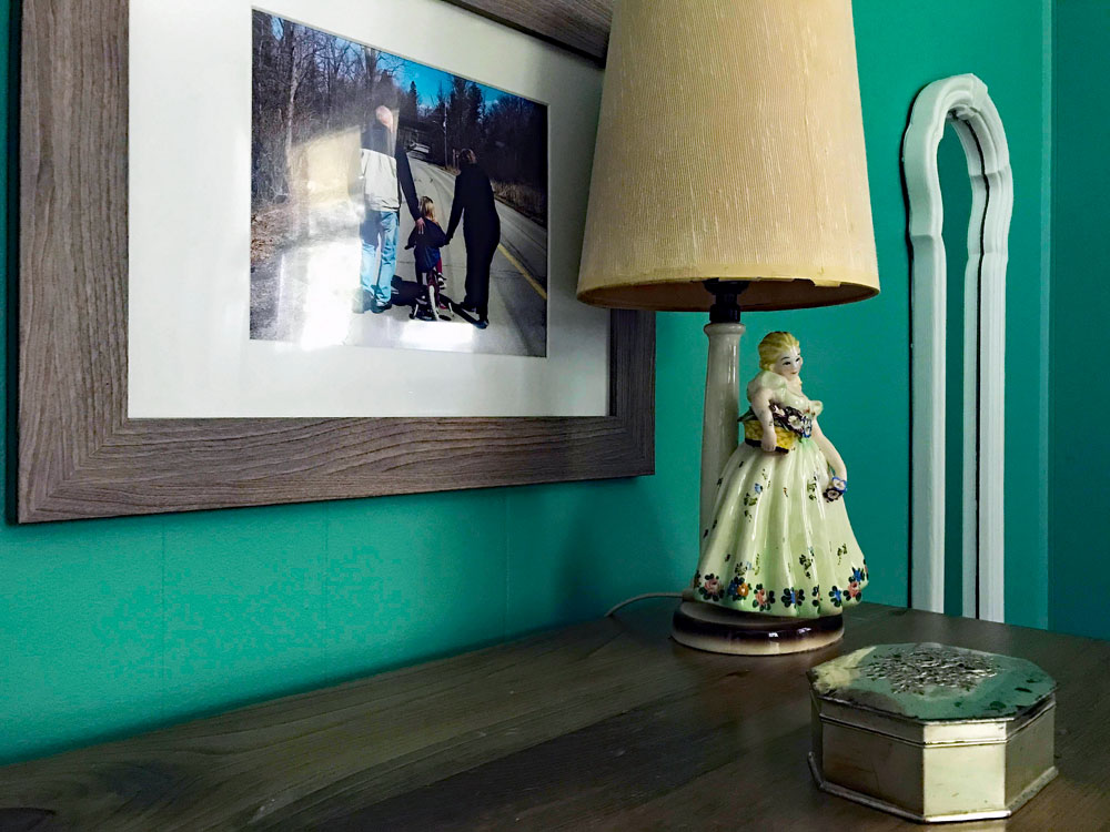 Woman statue lamp and silver box sitting on a dresser in front of a framed photo and mirror