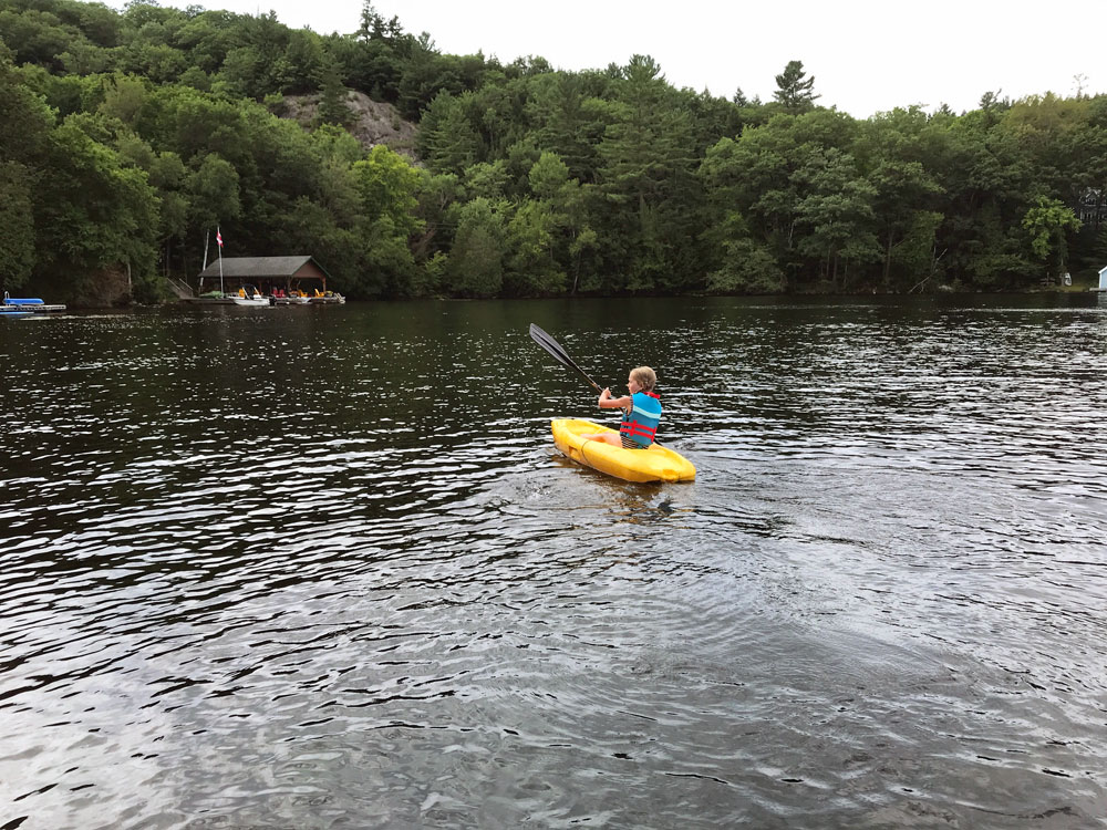 Child paddling a yellow kayak on a lake surrounded by trees